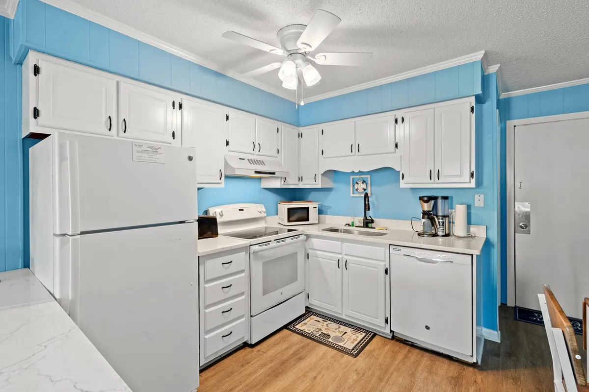 A welcoming kitchen and dining area with white cabinetry, blue walls, and a visible dining table. The space is prepped for both meal preparation and group dining, reflecting a warm, light-hearted atmosphere perfect for celebrations or everyday gatherings.