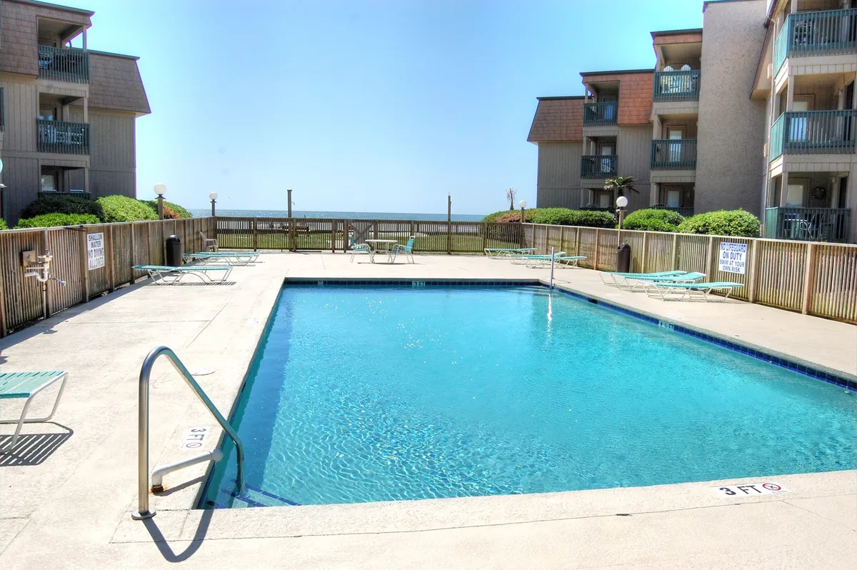 An inviting exterior view of the resort's swimming pool, surrounded by lounge chairs and the balconies of the surrounding buildings. The scene suggests a place for families to relax, swim, and enjoy time together just steps from their accommodation.