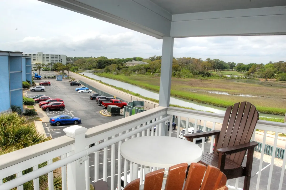 A cozy, private balcony with comfortable seating overlooking a calm waterway framed by lush greenery. The scene invites couples to relax with morning coffee or share a quiet conversation while taking in natural beauty.