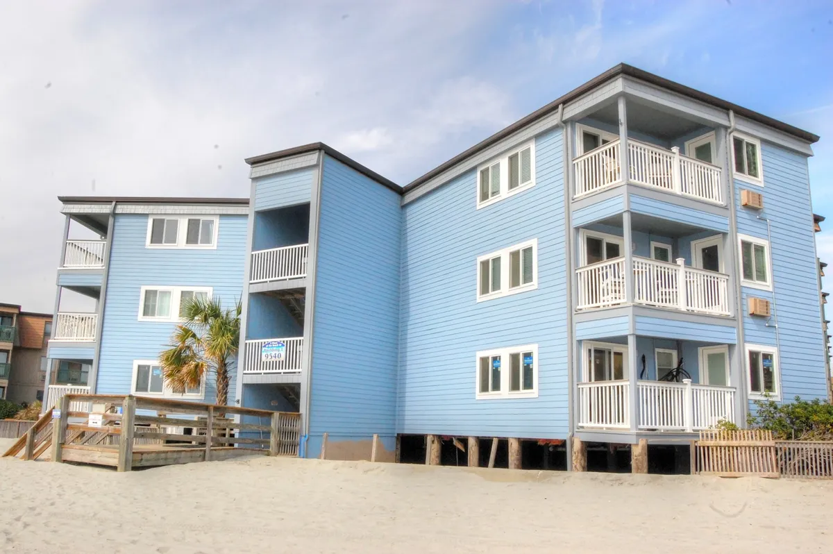 The photo showcases the blue exterior of the condo building with balconies and a prominent palm tree out front. It evokes the appeal of private outdoor space and hints at ocean views, underscoring the connection between the home base and the beachside lifestyle.